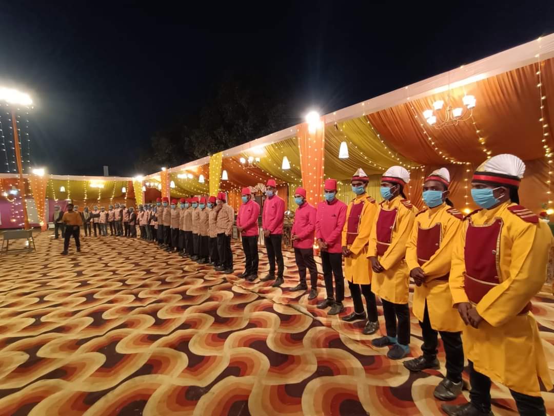 Service team lined up wearing yellow and pink traditional sherwanis with turbans