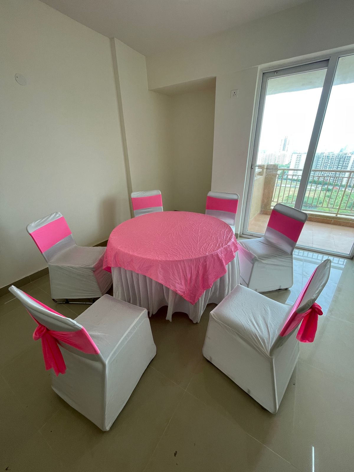 Round dining table laid with white linen and chairs finished with pink tie-back ribbons