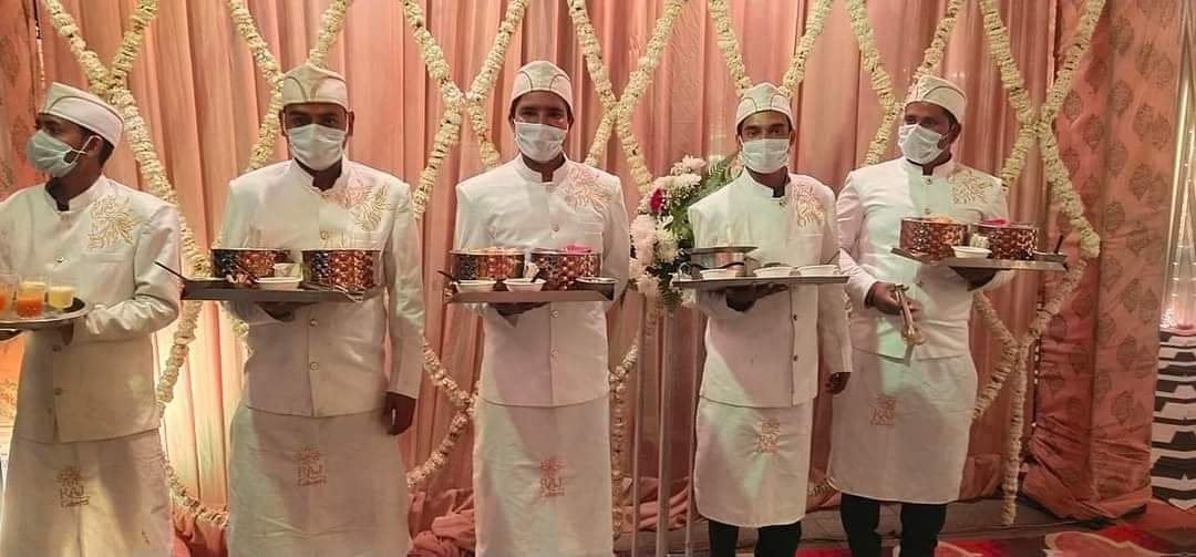 Service staff in white jackets and caps holding starter platters, waiting to pass them