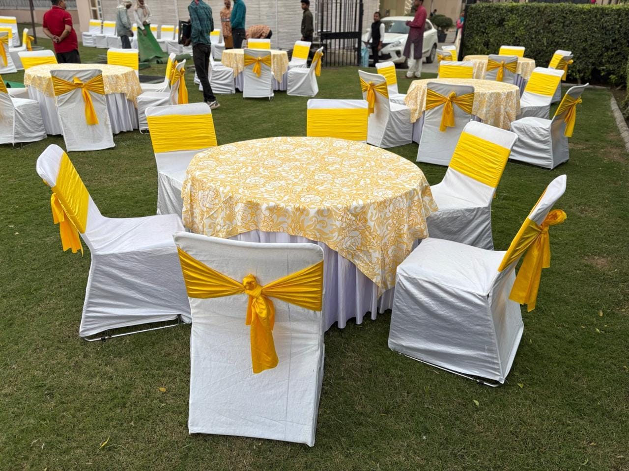 Round dining tables on a lawn dressed in yellow floral cloth with matching chair sashes