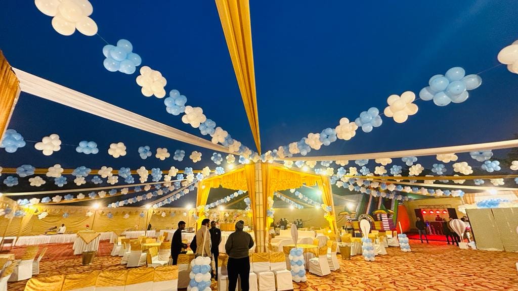 Outdoor banquet canopy at night with yellow drapes and hanging balloon clusters