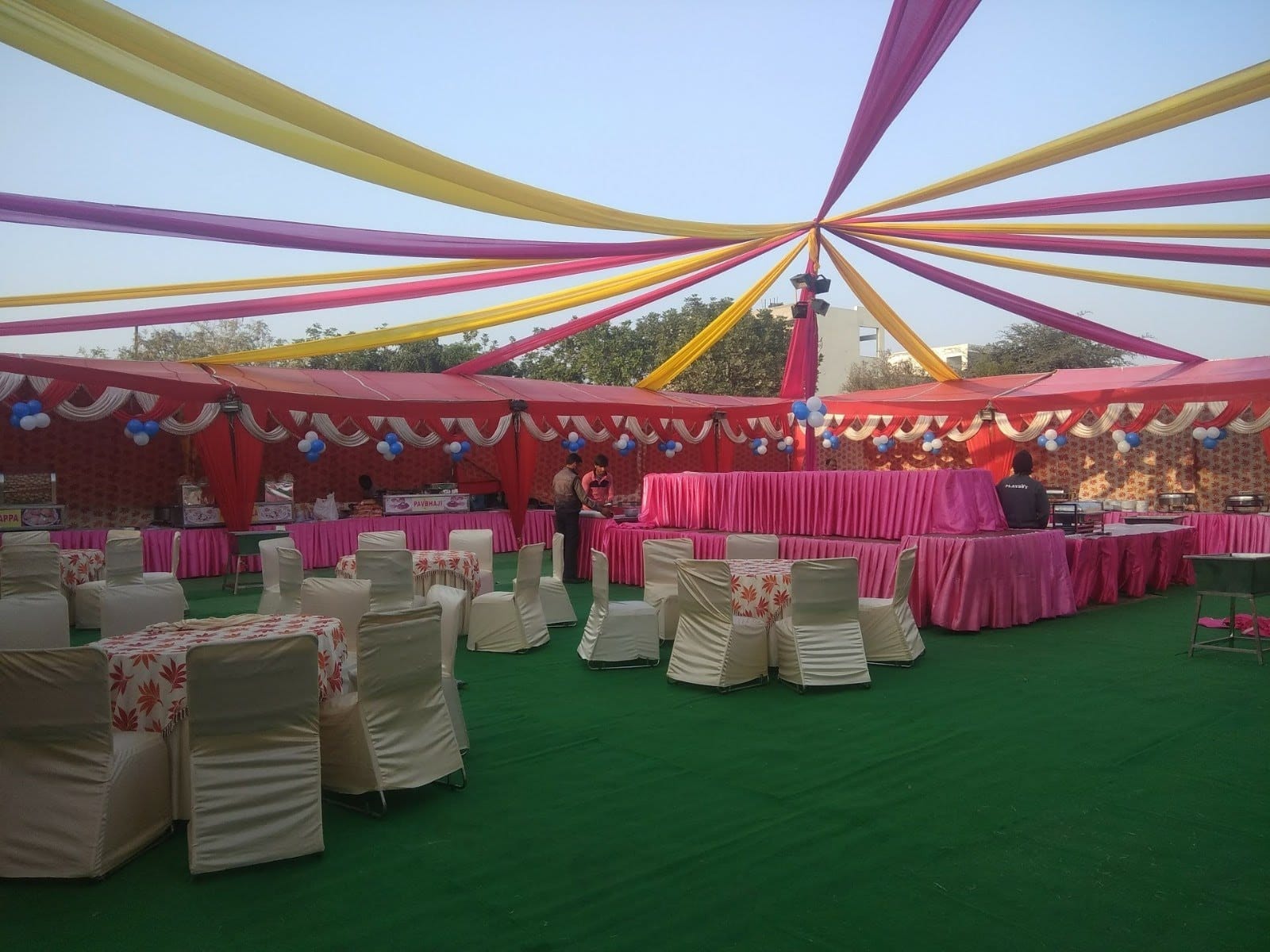 Open lawn setup with canopy rays overhead, dining tables laid out and buffet stalls along one side