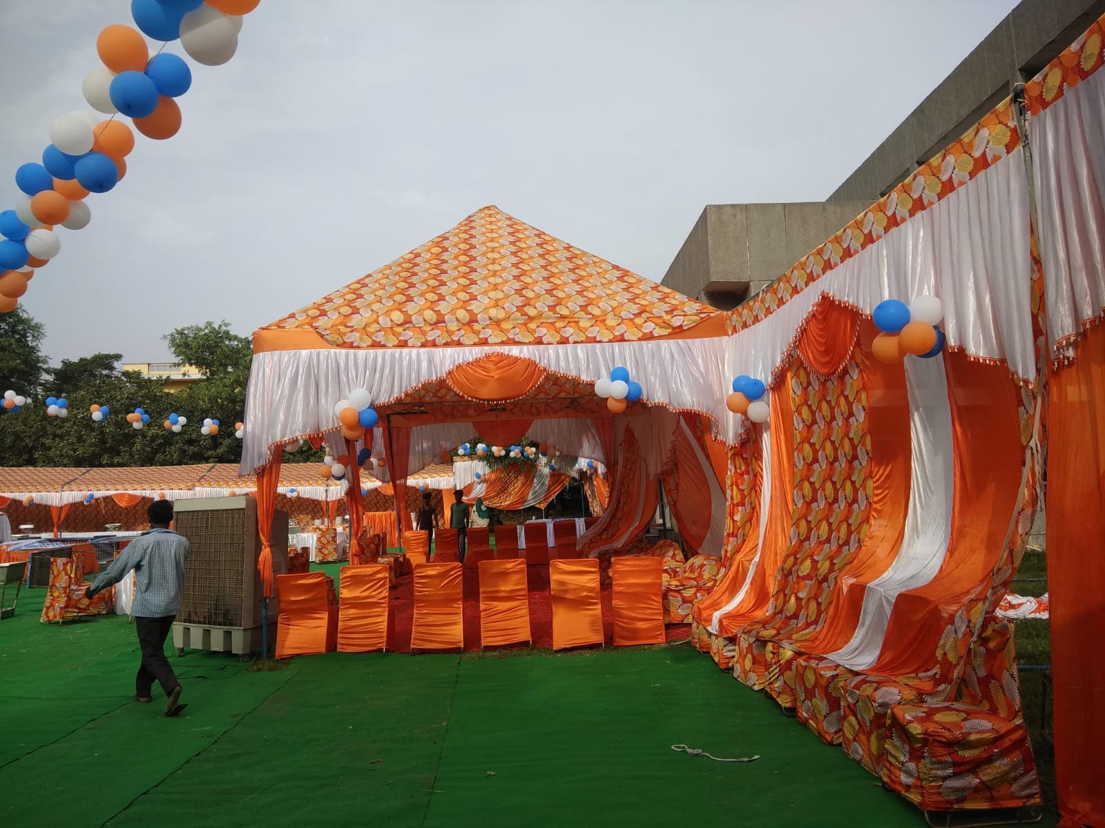 An orange and white shamiana put up by the Bittu Caterers team, with matching chair covers set out on green matting