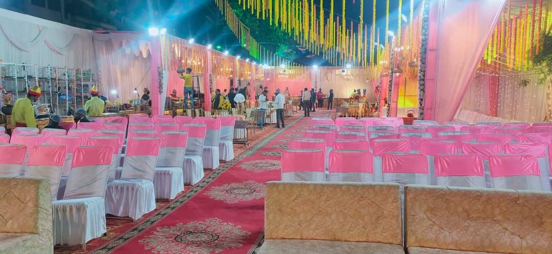 Wedding hall seating with pink chair sashes, a red carpet aisle and marigold strings hanging overhead